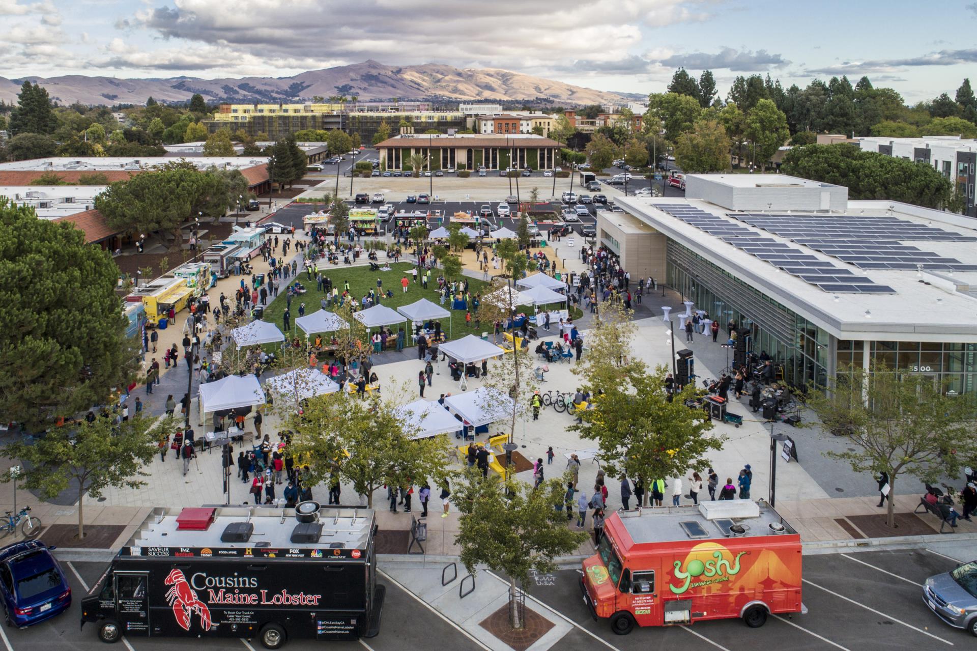 View of community gathering with food trucks and the Downtown event center including a roof full of solar panels with hills in the background